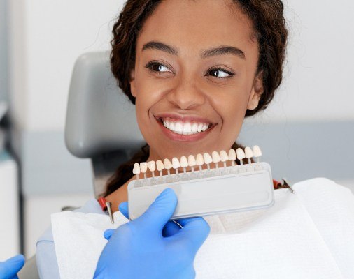 Woman's smile compared with porcelain veneer shades during cosmetic dentistry visit