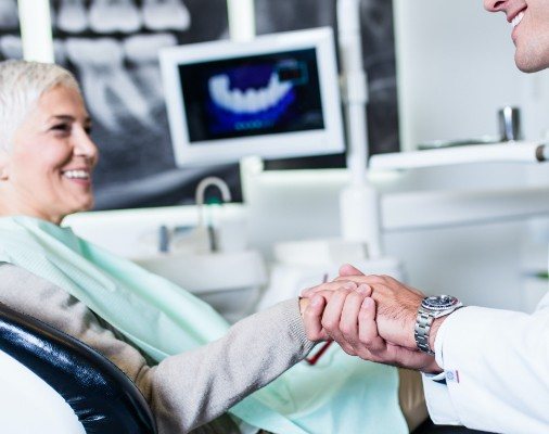Woman shaking hands with dentist during dental implant consultation