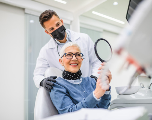 An older woman admiring her new dental implant with a hand mirror