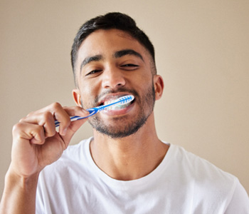 A young man brushing his teeth against a studio background