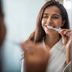 Woman looking in the mirror while brushing her teeth