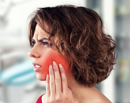 Woman in need of root canal therapy holding cheek in pain