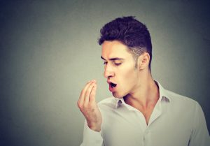 man smelling breath with hand