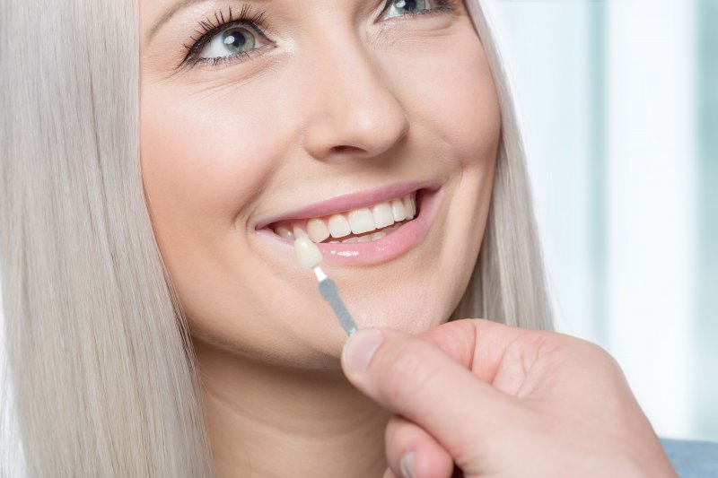 a young woman smiling while a dentist uses a shade guide to determine the color of her veneers