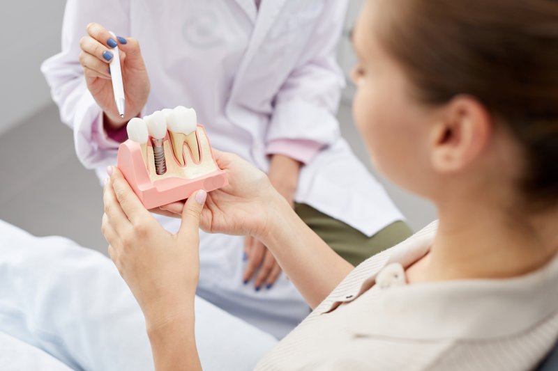 a dentist showing a patient a cross-section mouth mold that contains a dental implant
