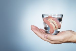 hand holding glass of water with soaking dentures  