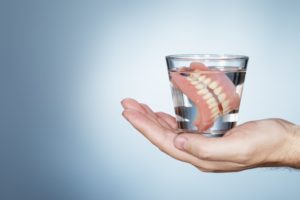hand holding glass of water with soaking dentures